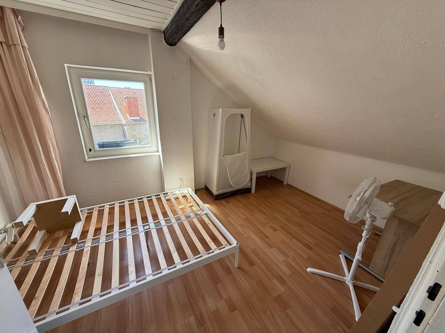 Schlafzimmer im Dachgeschoss mit Bettgestell, Dachschräge und Fenster für natürliches Licht.
