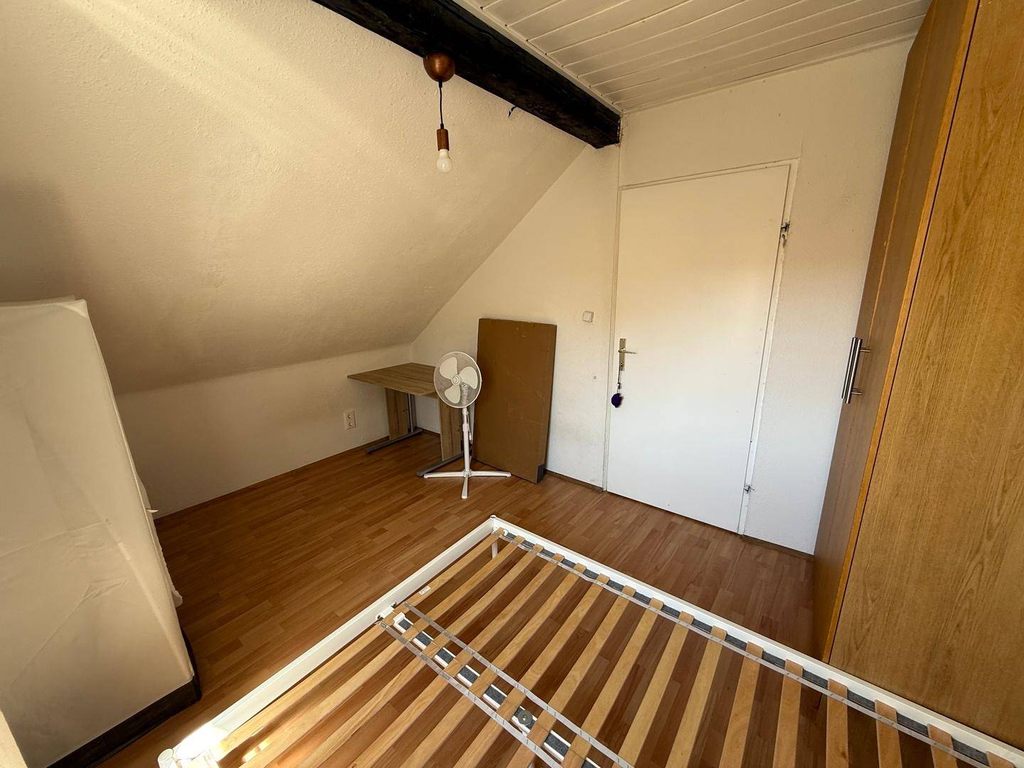 Schlafzimmer mit Bettgestell, Schreibtisch und Kleiderschrank unter der Dachschräge.