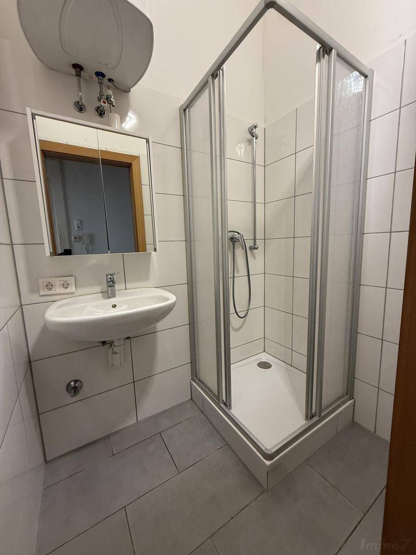 Funktionales Badezimmer mit Duschkabine, Waschbecken, Spiegelschrank und Wandfliesen in hellem Design.