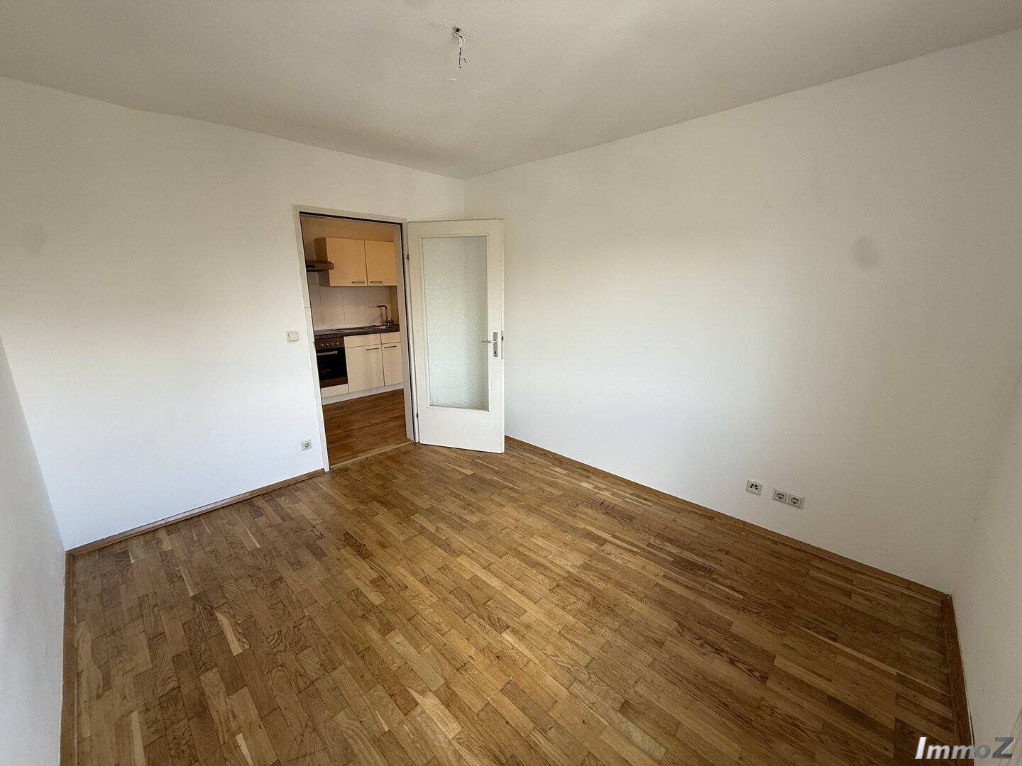Geräumiger Raum mit Holzboden und direktem Zugang zu einer kleinen Küche.
