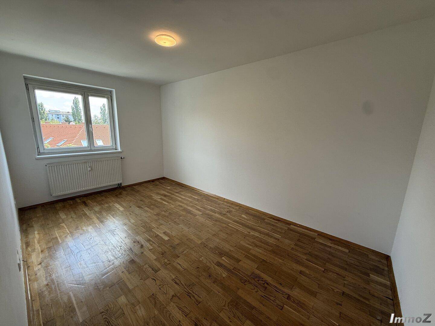 Helles Schlafzimmer mit Holzboden und Fenster, das einen Blick nach draußen bietet.