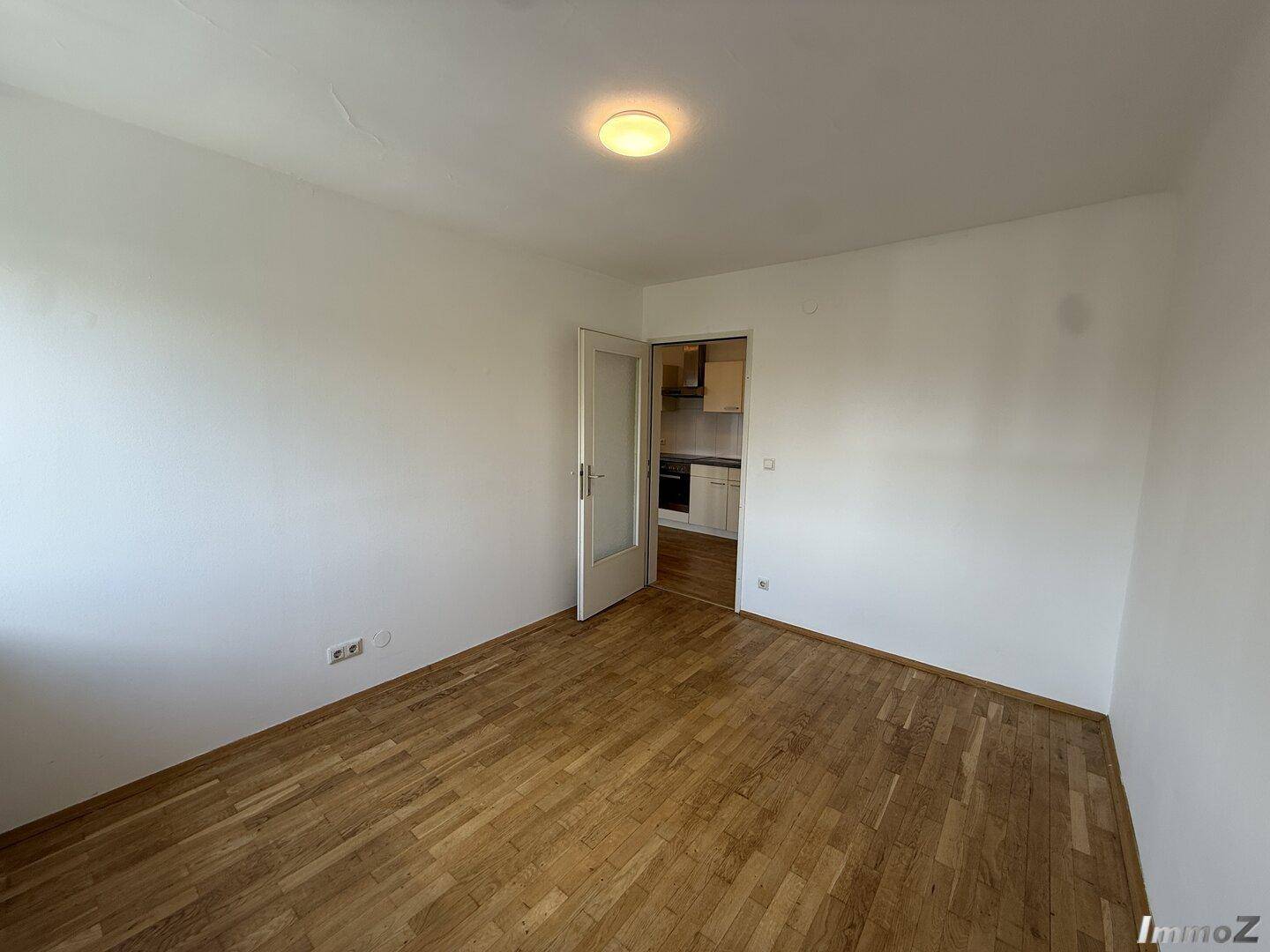 Heller Raum mit Holzboden und Zugang zu einer angrenzenden Küchenzeile.