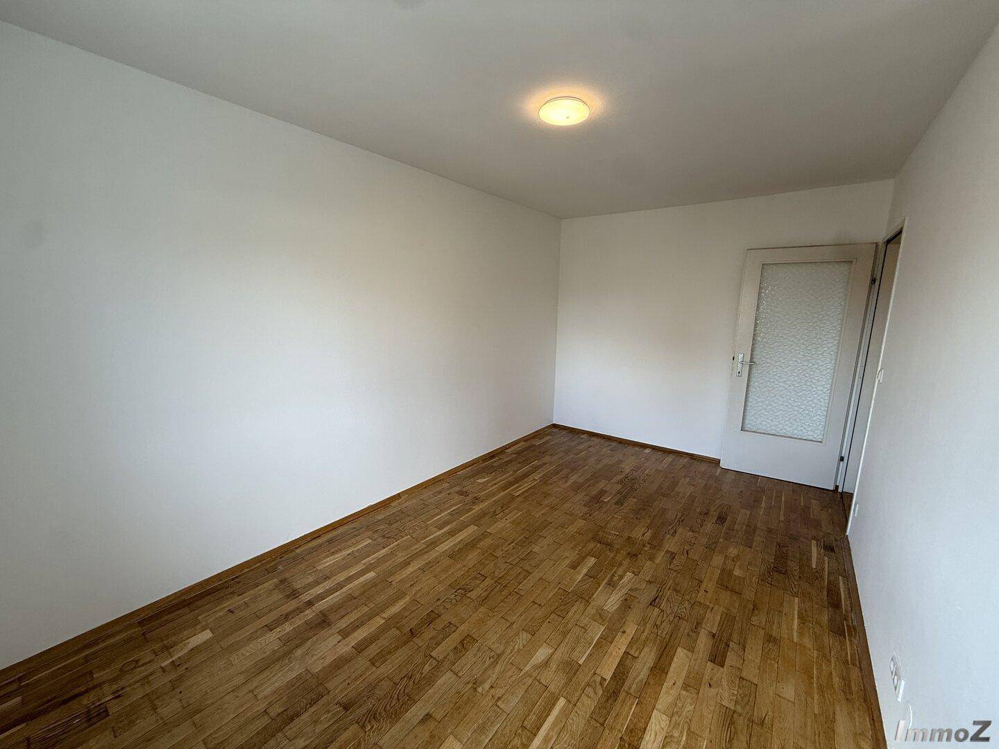 Schlichtes Schlafzimmer mit Holzboden und weiß gestrichenen Wänden, ideal für individuelle Gestaltung.