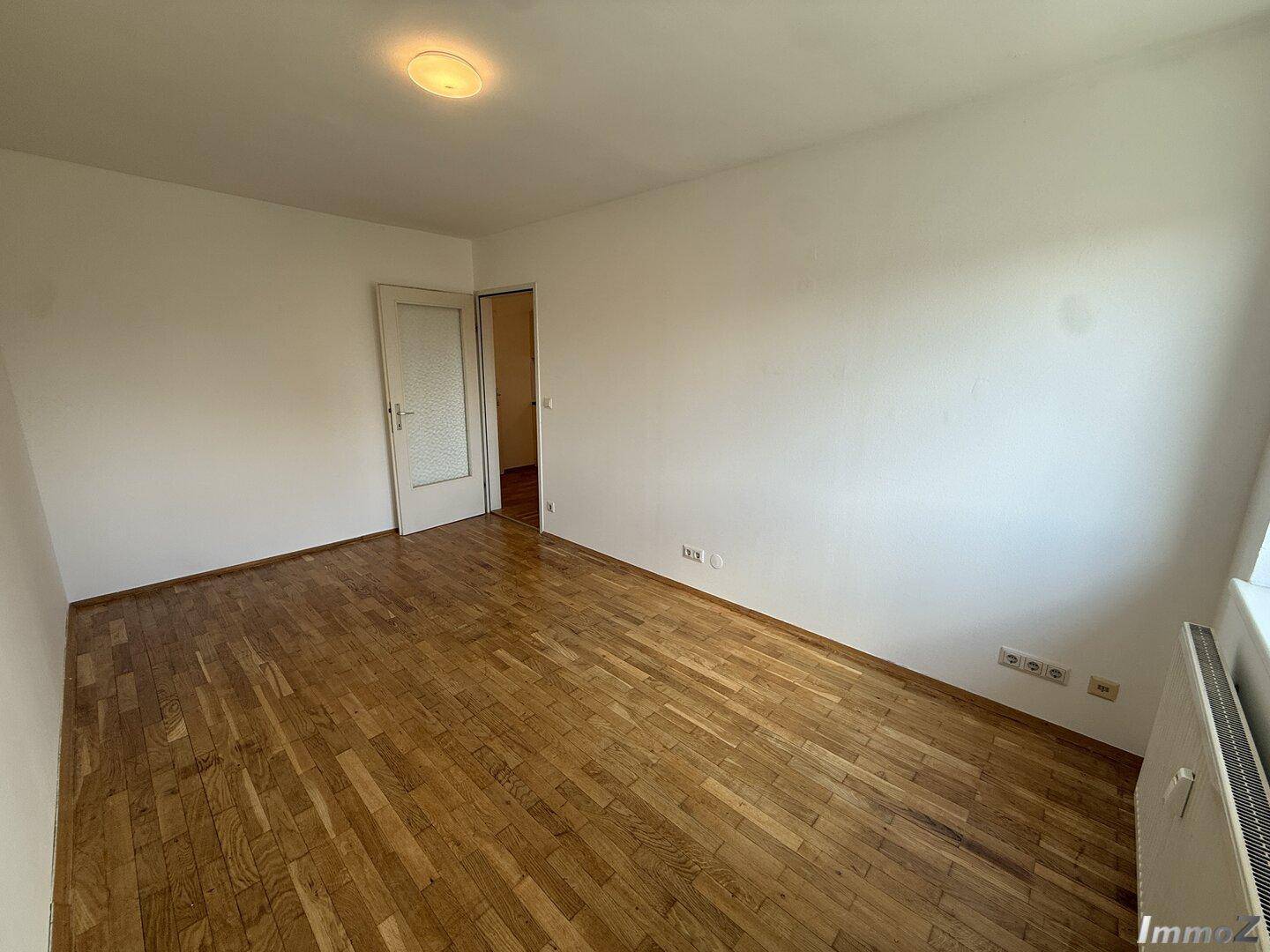 Leerer Wohnraum mit Holzboden und weiß gestrichenen Wänden, bereit zur Einrichtung.