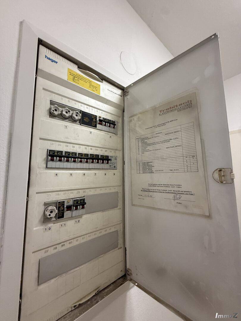 Offener elektrischer Sicherungskasten mit verschiedenen Schaltern und Beschriftungen an der Wand.