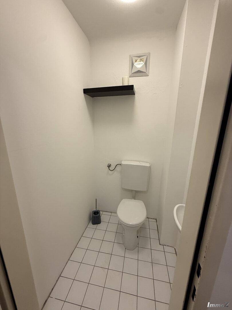 Kleines separates WC mit Toilette, Fliesenboden und Wandregal, ohne Waschbecken.