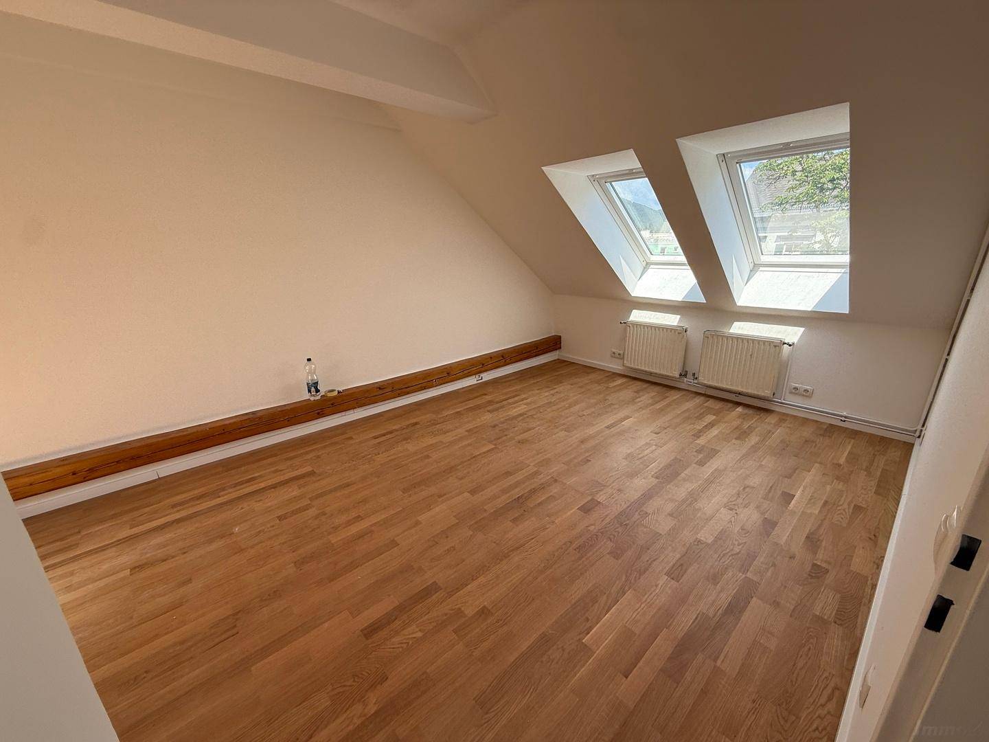 Geräumiges Dachzimmer mit Holzboden, weißen Wänden und zwei Dachfenstern für viel Tageslicht.