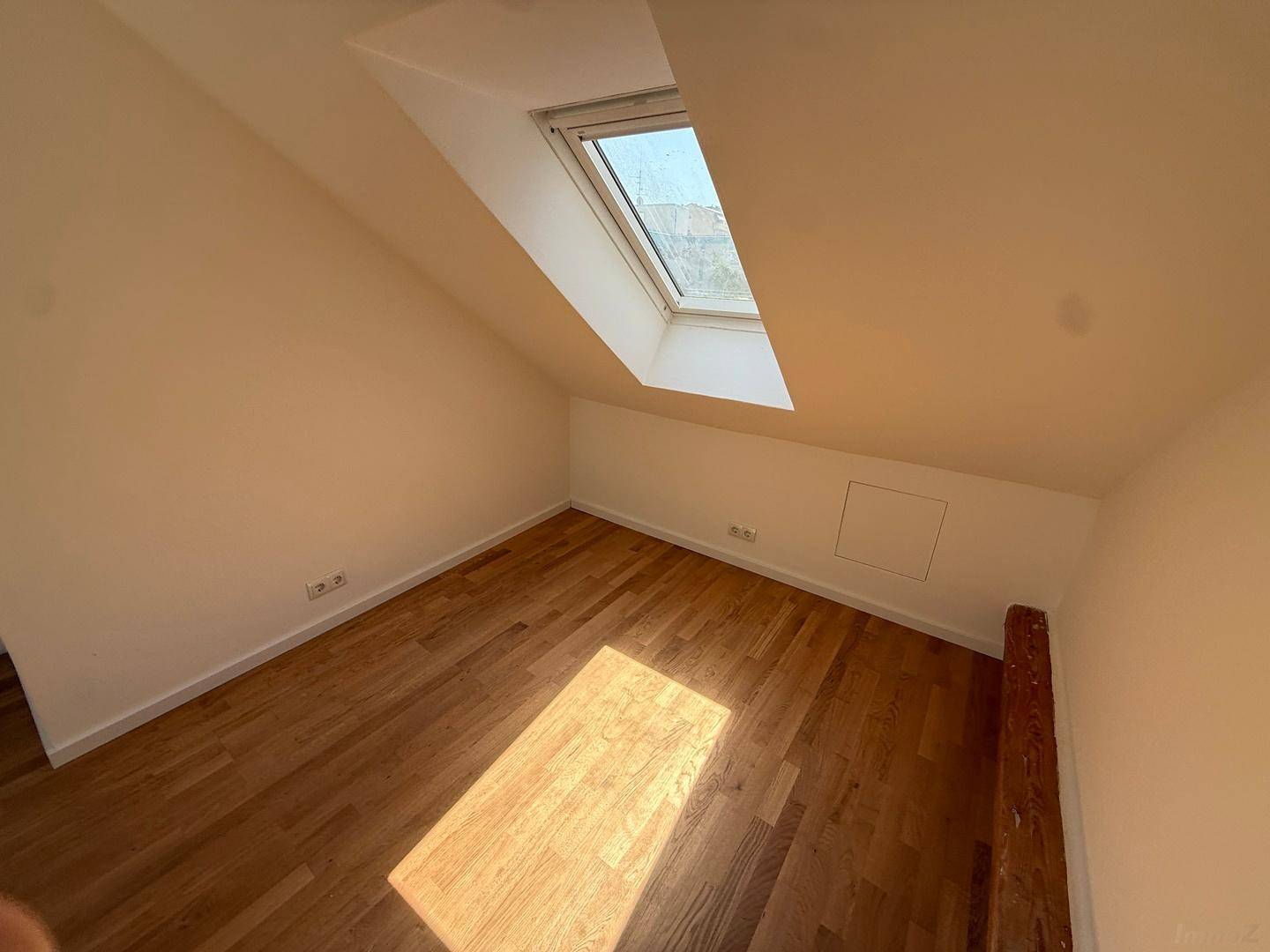 Lichtdurchflutetes Dachzimmer mit Holzboden und schrägen Wänden, ideal als Schlaf- oder Arbeitszimmer.