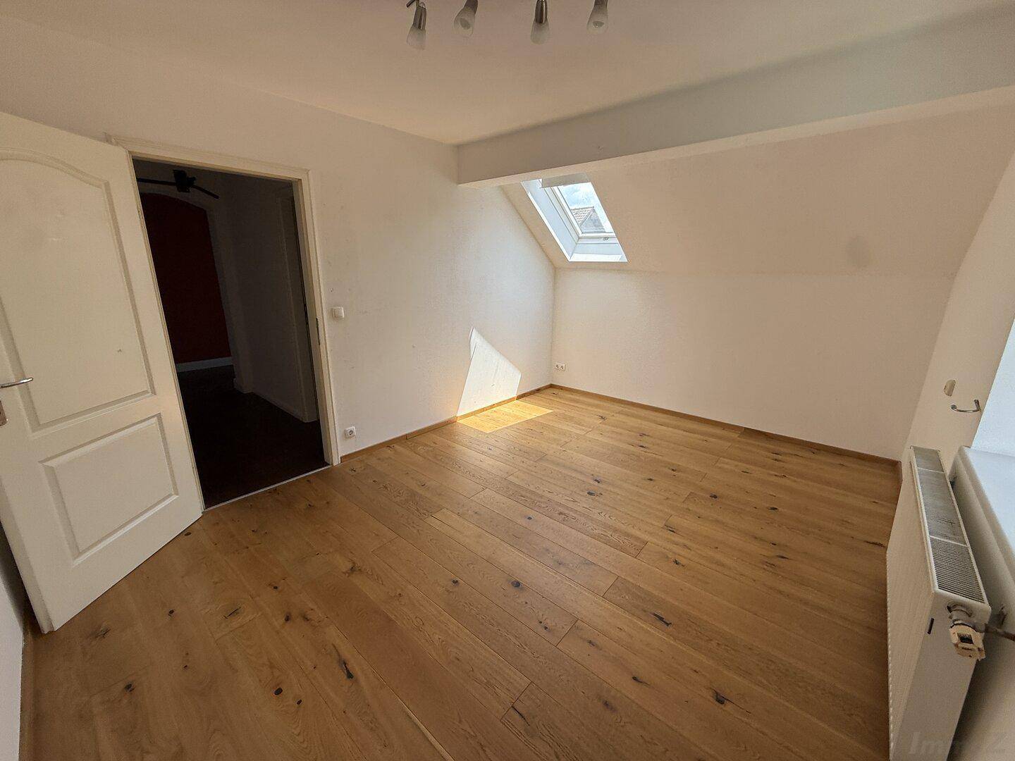 Helles Schlafzimmer mit Holzboden, Dachschräge und einem Dachfenster für natürliches Licht.