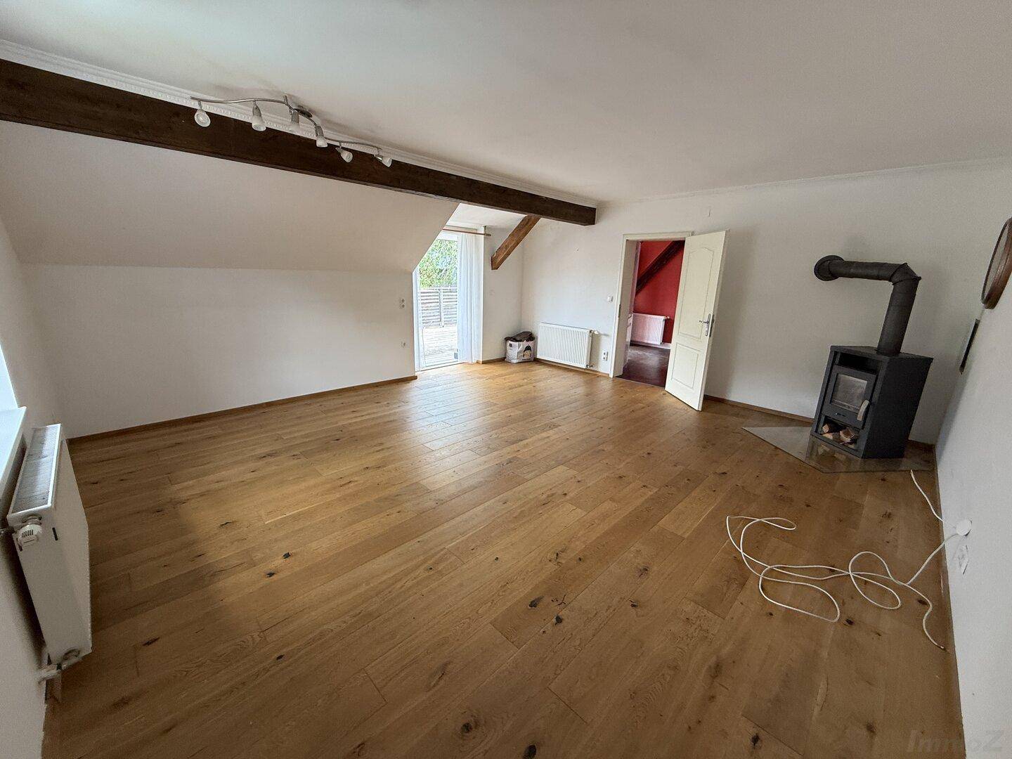 Geräumiges Wohnzimmer mit Holzboden, freiliegenden Balken und einem Holzofen.