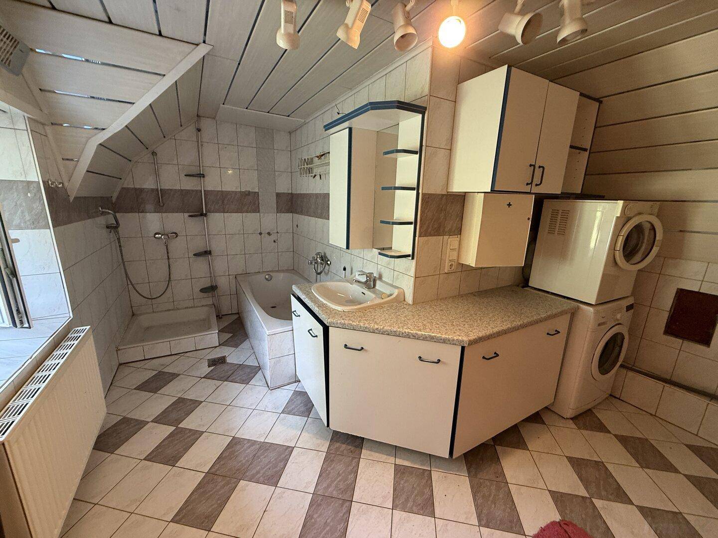 Badezimmer mit Badewanne, Dusche, Waschbecken und Waschmaschine unter Dachschrägen.