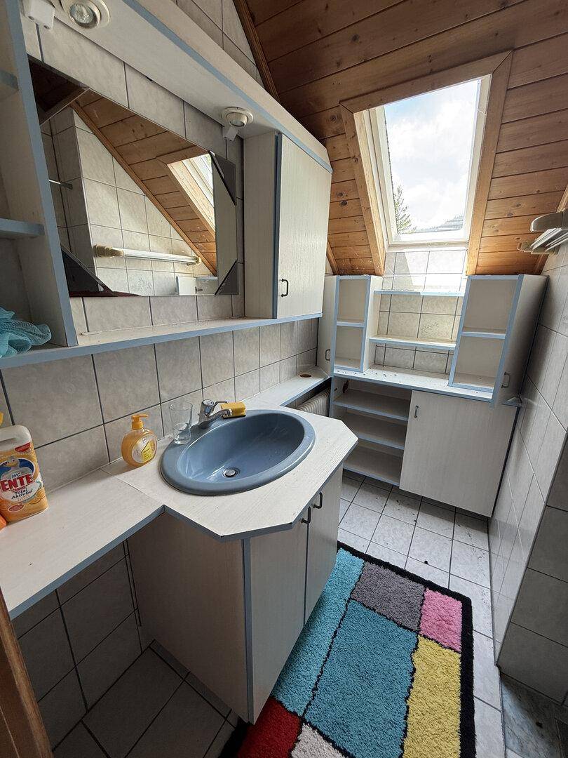Badezimmer mit Dachfenster, Waschbecken und Spiegelschrank unter einer Holzdecke.
