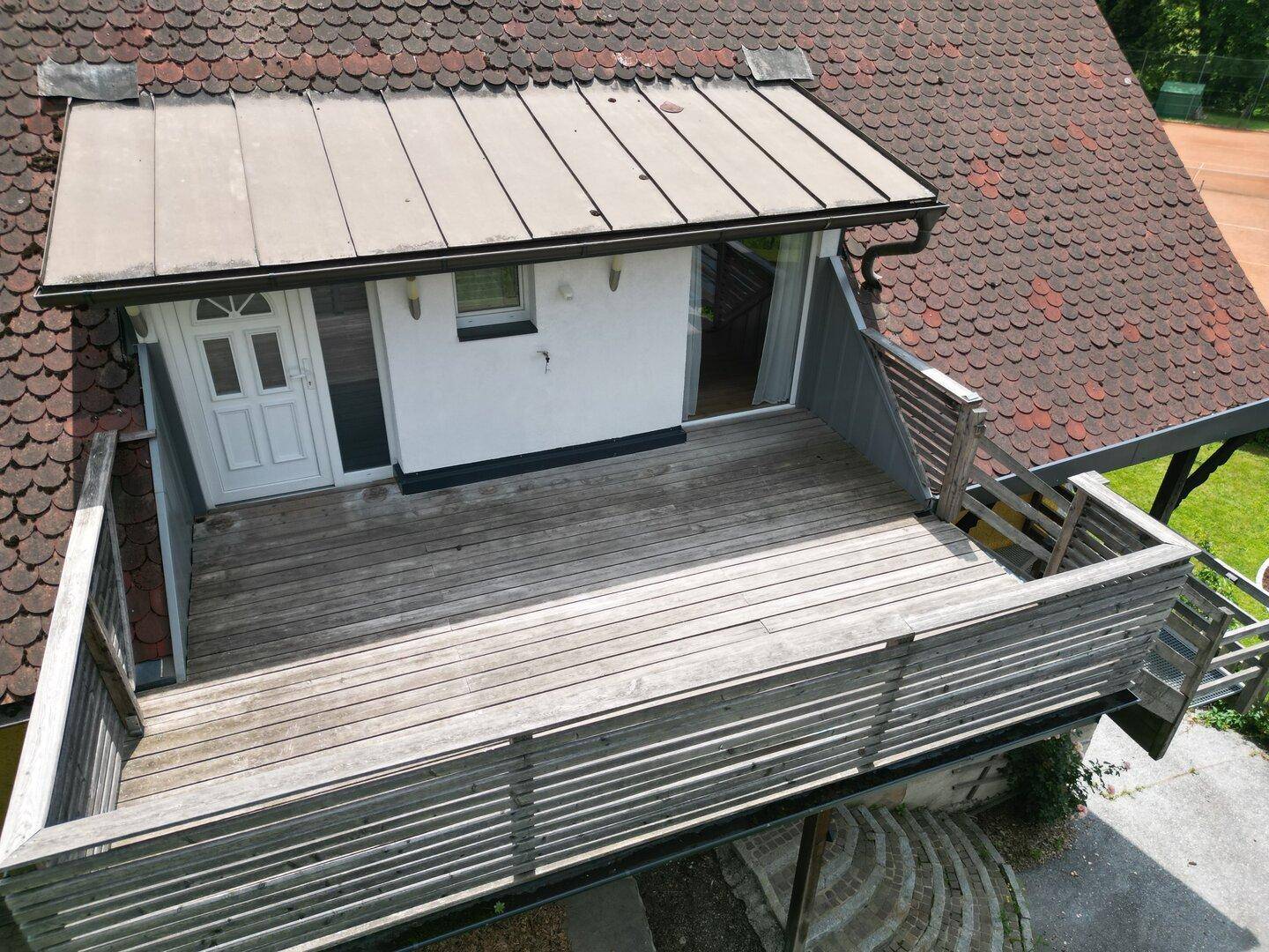 Geräumige Holzterrasse mit Geländer und Zugang zu einem Zimmer, ideal zum Entspannen.