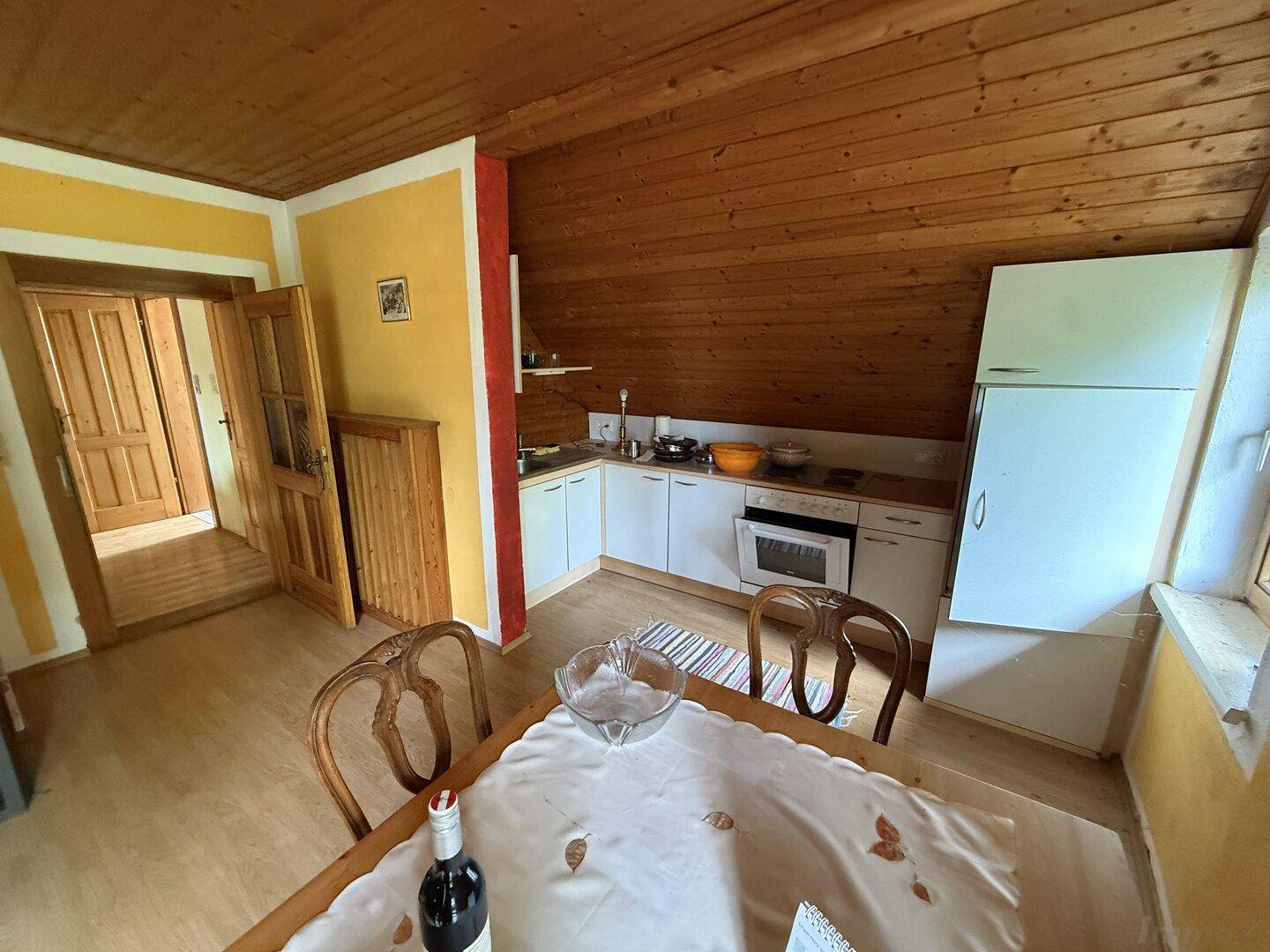 Kleine Küche mit Essbereich, Holzwänden und Dachschrägen in einem gemütlichen Ambiente.