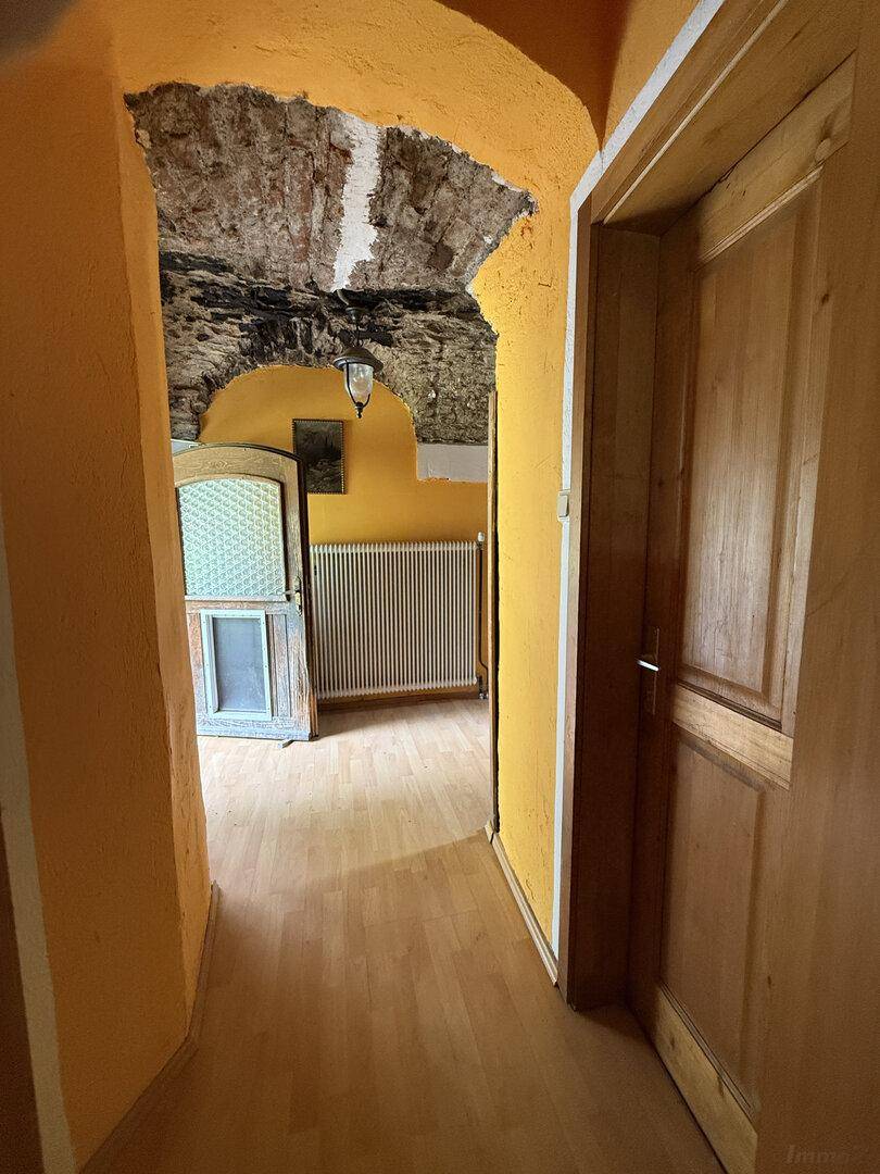 Gelber Flur mit Holzboden und einem freigelegten Gewölbe aus Naturstein an der Decke.