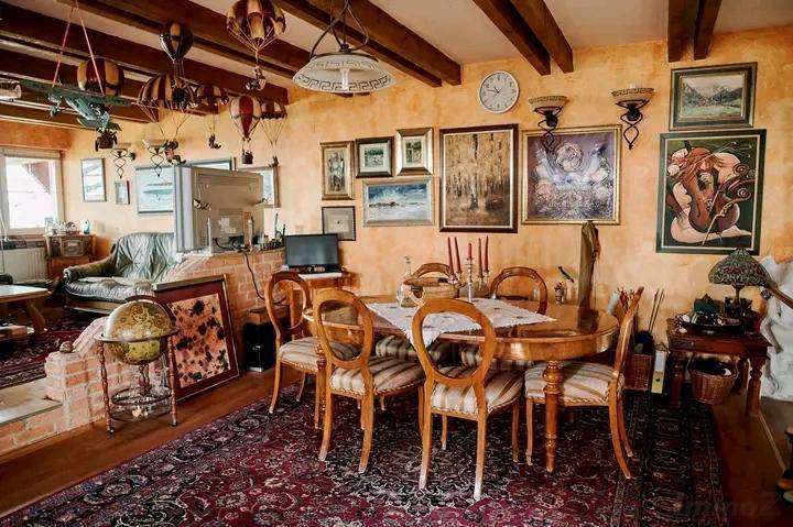 Rustikaler Wohn- und Essbereich mit Holzbalken, Kamin und vielen Bildern an den orangefarbenen Wänden.