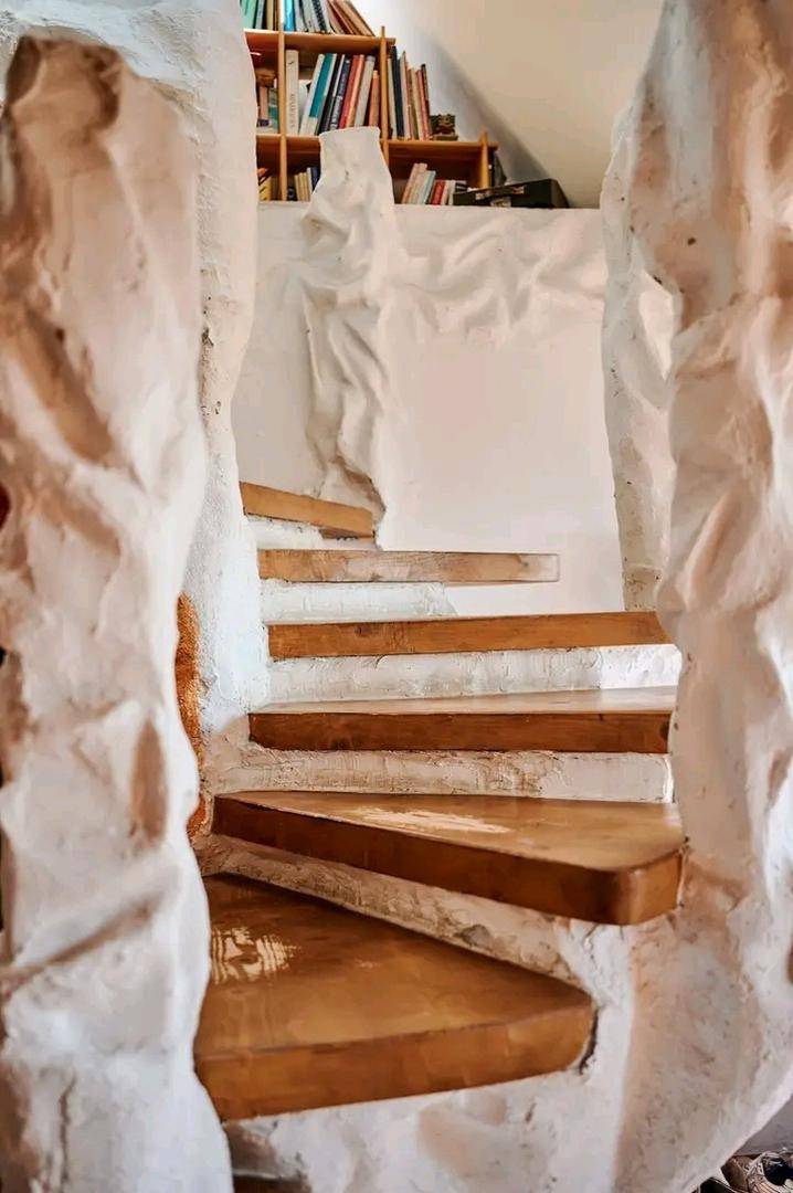 Einzigartige Holztreppe mit skulpturalen, weißen Wänden, die zu einem oberen Bereich führt.