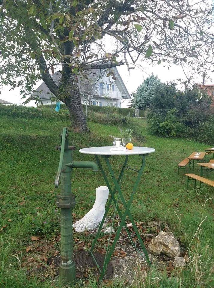 Gartenbereich mit alter Wasserpumpe, kleinem Tisch und einem traditionellen Haus im Hintergrund.