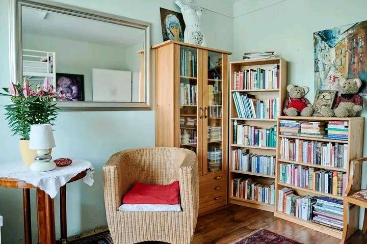Gemütlicher Wohnbereich mit Korbsessel, Bücherregalen und einem großen Spiegel an der hellgrünen Wand.