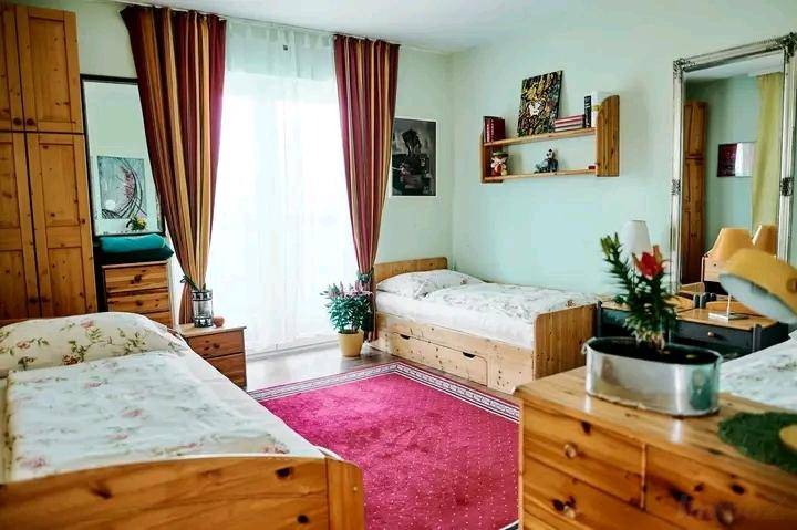 Helles Schlafzimmer mit zwei Einzelbetten, Holzmöbeln und einem großen Fenster mit Vorhängen.