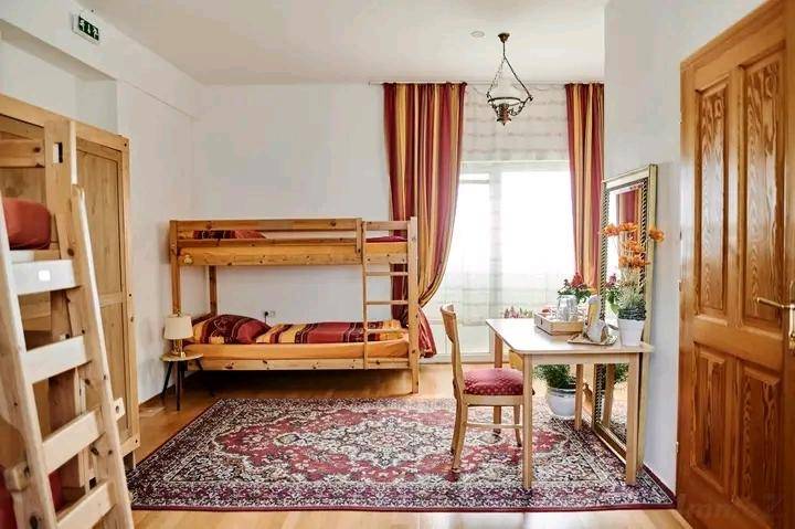 Schlafzimmer mit Etagenbett, Holzboden und einem Schreibtisch am Fenster, dekoriert mit einem Teppich.