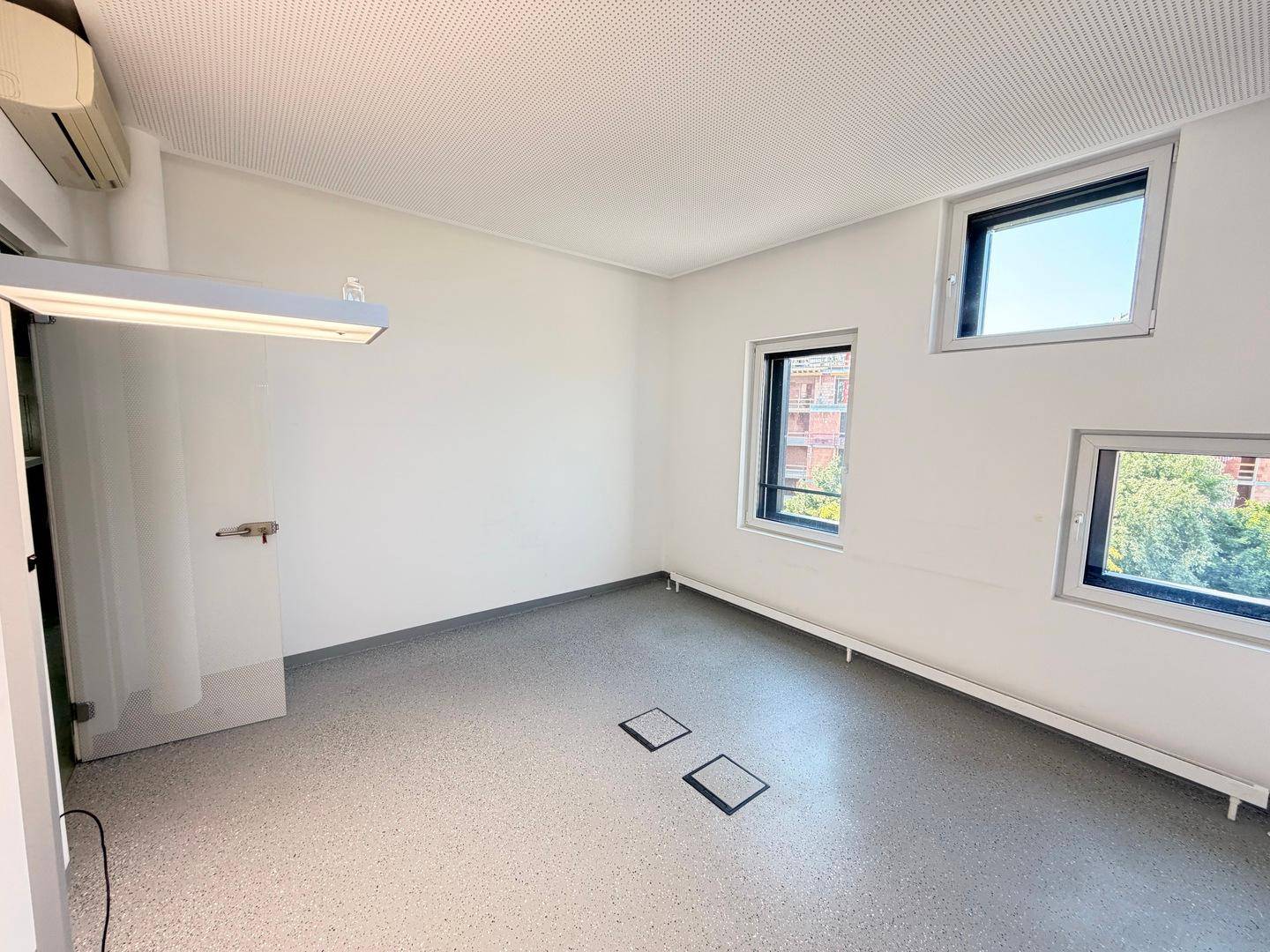 Leerer Büroraum mit Klimaanlage, mehreren Fenstern und praktischen Bodensteckdosen für flexible Nutzung.