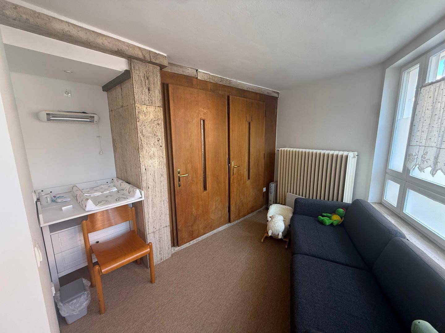 Kinderzimmer oder Wickelraum mit Wickeltisch, Sofa und großen Fenstern, hell und funktional.