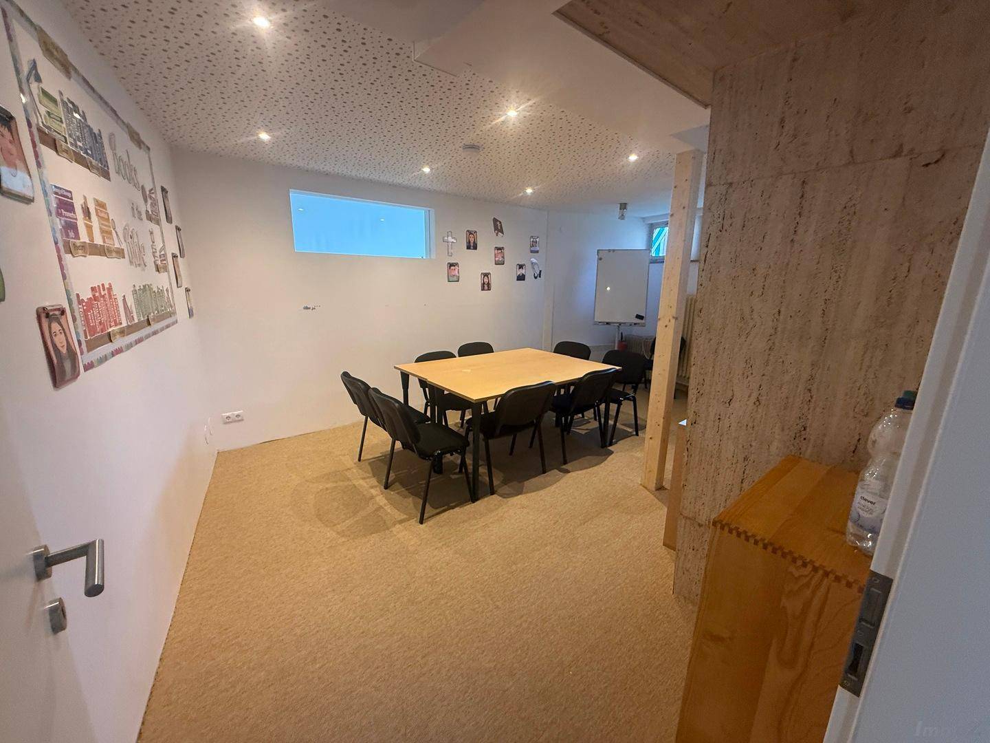 Besprechungsraum mit Teppichboden, Holztisch und Stühlen, dekoriert mit Bildern an der Wand.