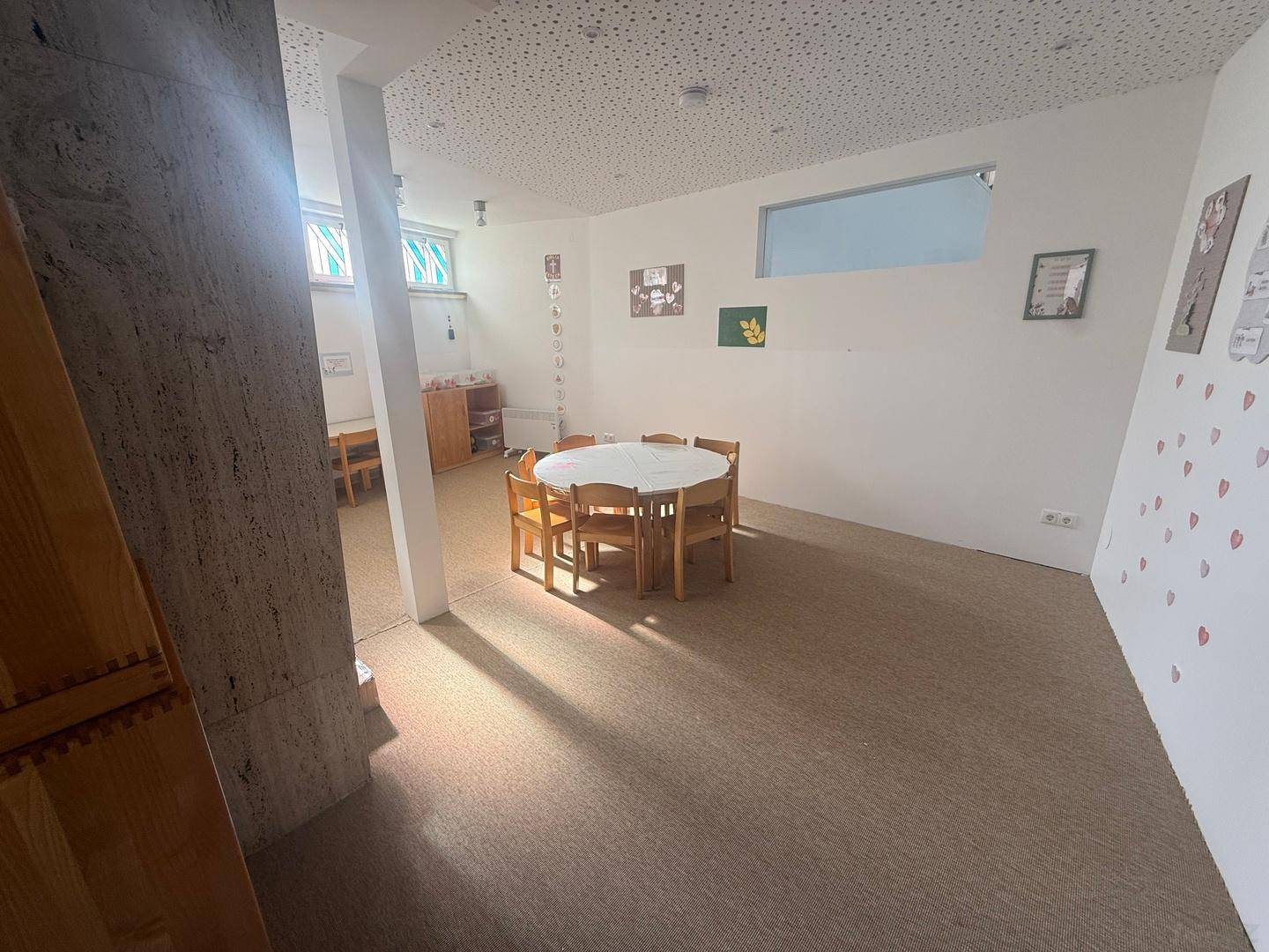 Heller Mehrzweckraum mit Teppichboden, Kindermöbeln und natürlichem Lichteinfall, ideal für Kinder.