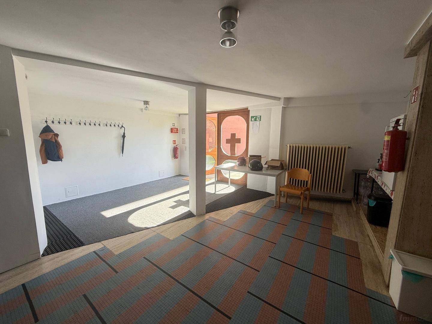 Heller Eingangsbereich mit Garderobe, gemustertem Teppichboden und Blick zur Eingangstür.