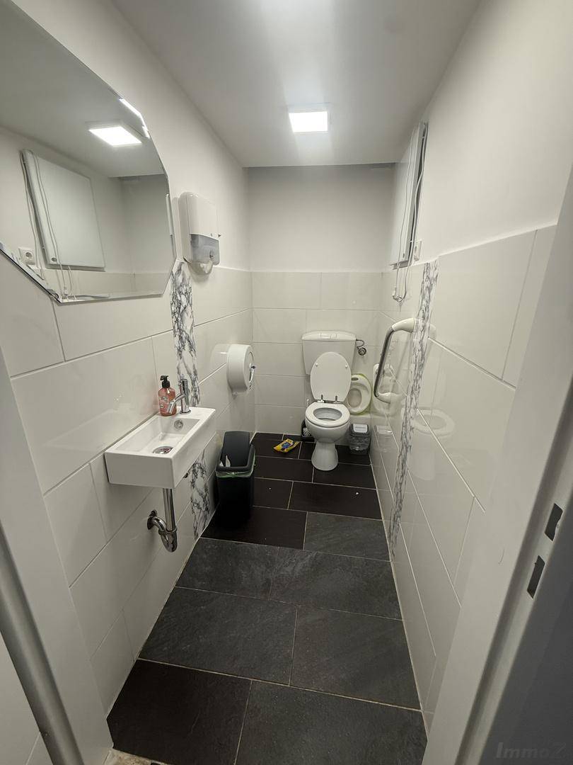Modern geflieste Toilette mit Waschbecken, WC und Haltegriffen für Barrierefreiheit, sauber und hell.