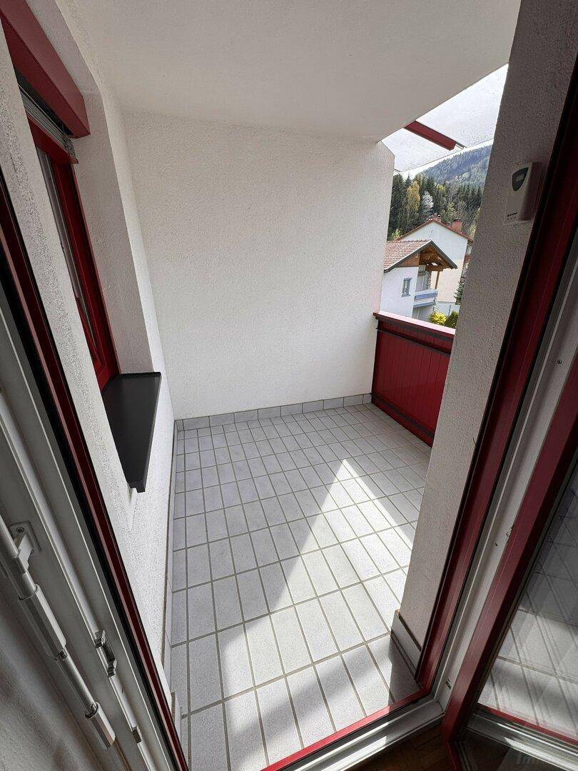 Heller Balkon mit Fliesenboden und rotem Geländer, bietet Platz für Entspannung.