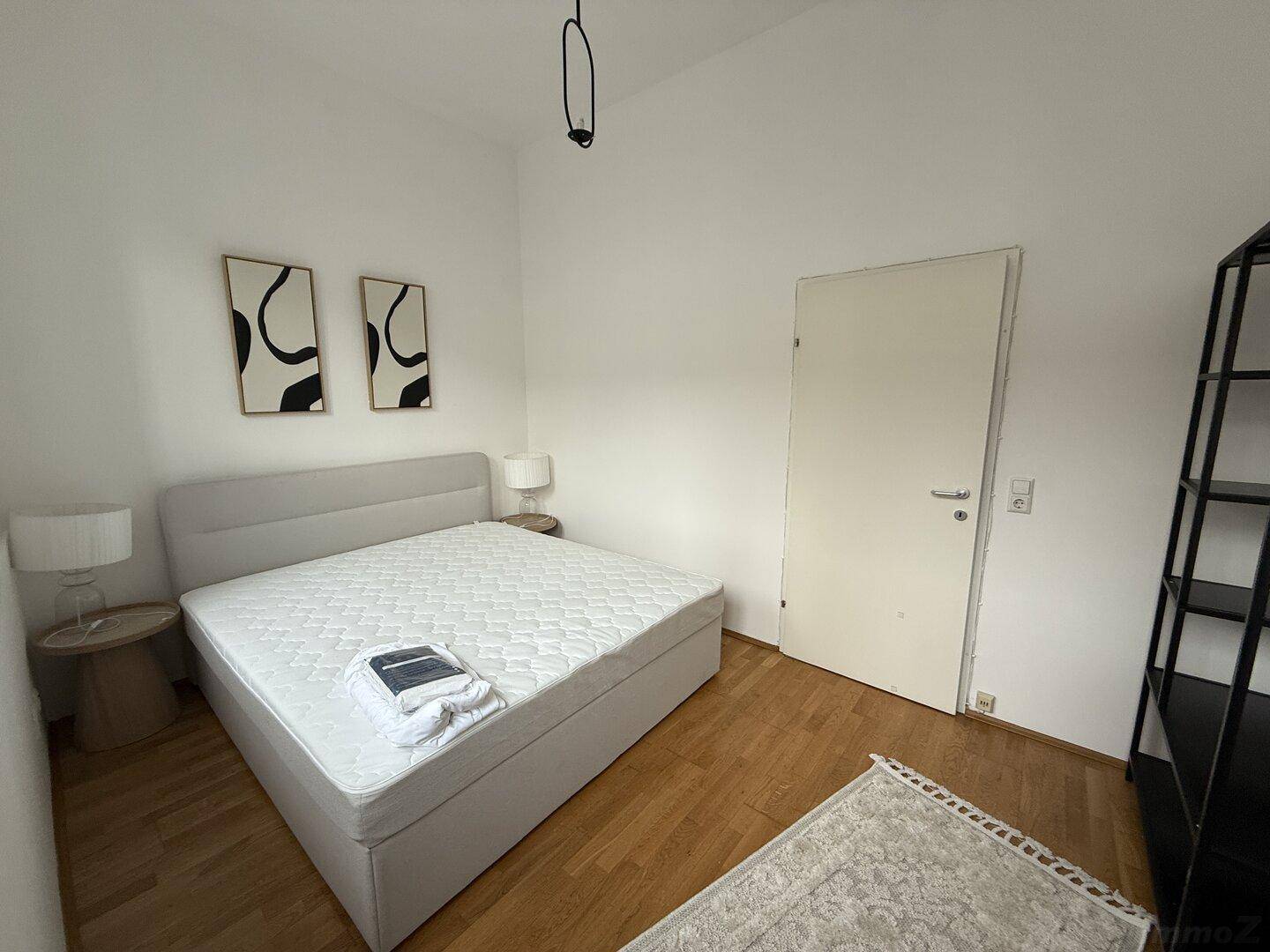 Helles Schlafzimmer mit Doppelbett, Nachttischen und schlichter Wanddekoration.