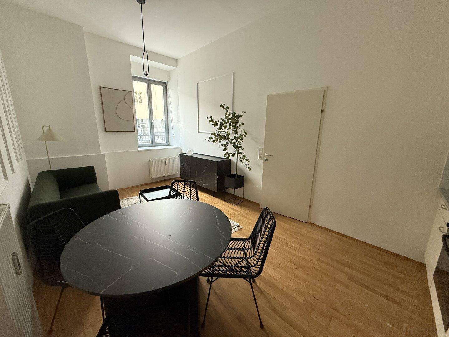 Gemütlicher Wohn- und Essbereich mit Holzboden, modernem Esstisch und Blick auf die Straße.