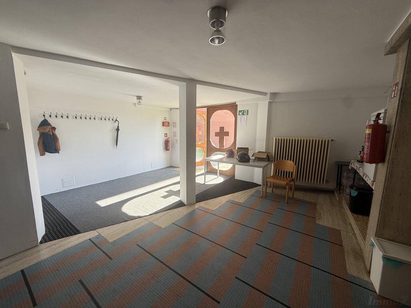 Heller Eingangsbereich mit Garderobe, Heizkörper und gemustertem Teppichboden.