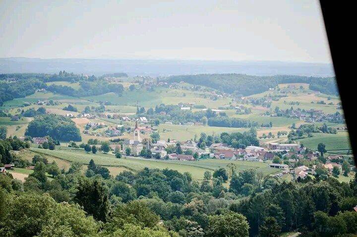 Panoramablick auf ein idyllisches Dorf, eingebettet in eine grüne, hügelige Landschaft.