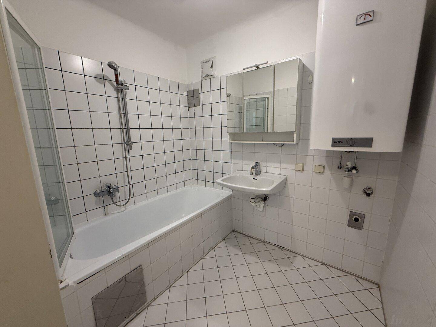 Badezimmer mit Badewanne, Duschvorrichtung und weißen Fliesen, inklusive Spiegelschrank.
