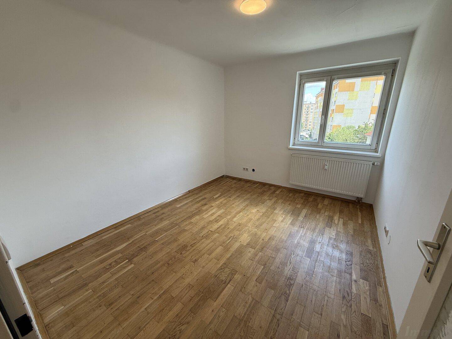 Leeres Zimmer mit Holzparkettboden und Fenster, das viel Tageslicht hereinlässt.