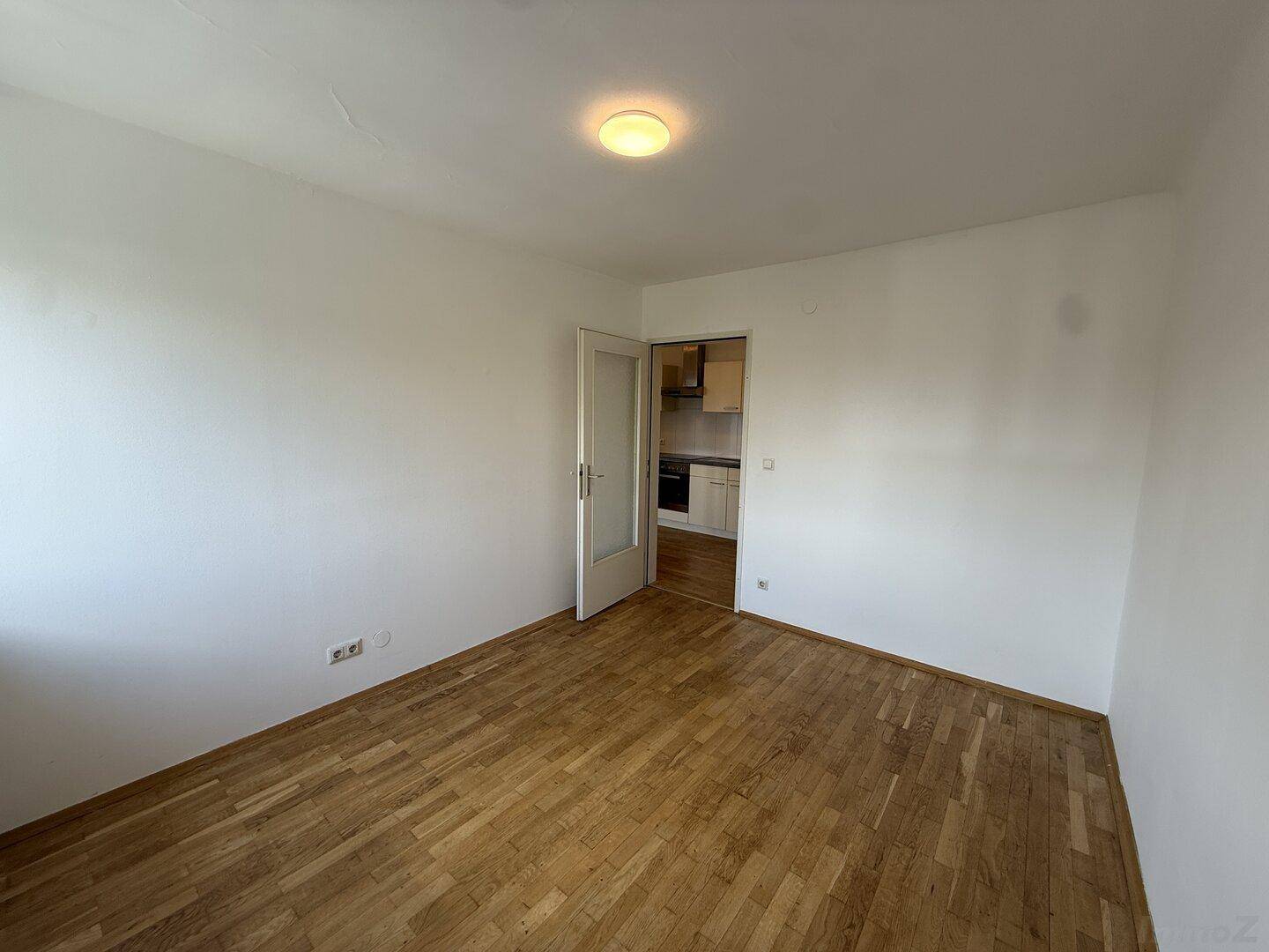 Heller Raum mit Holzparkettboden und Zugang zu einer kleinen Küchenzeile.