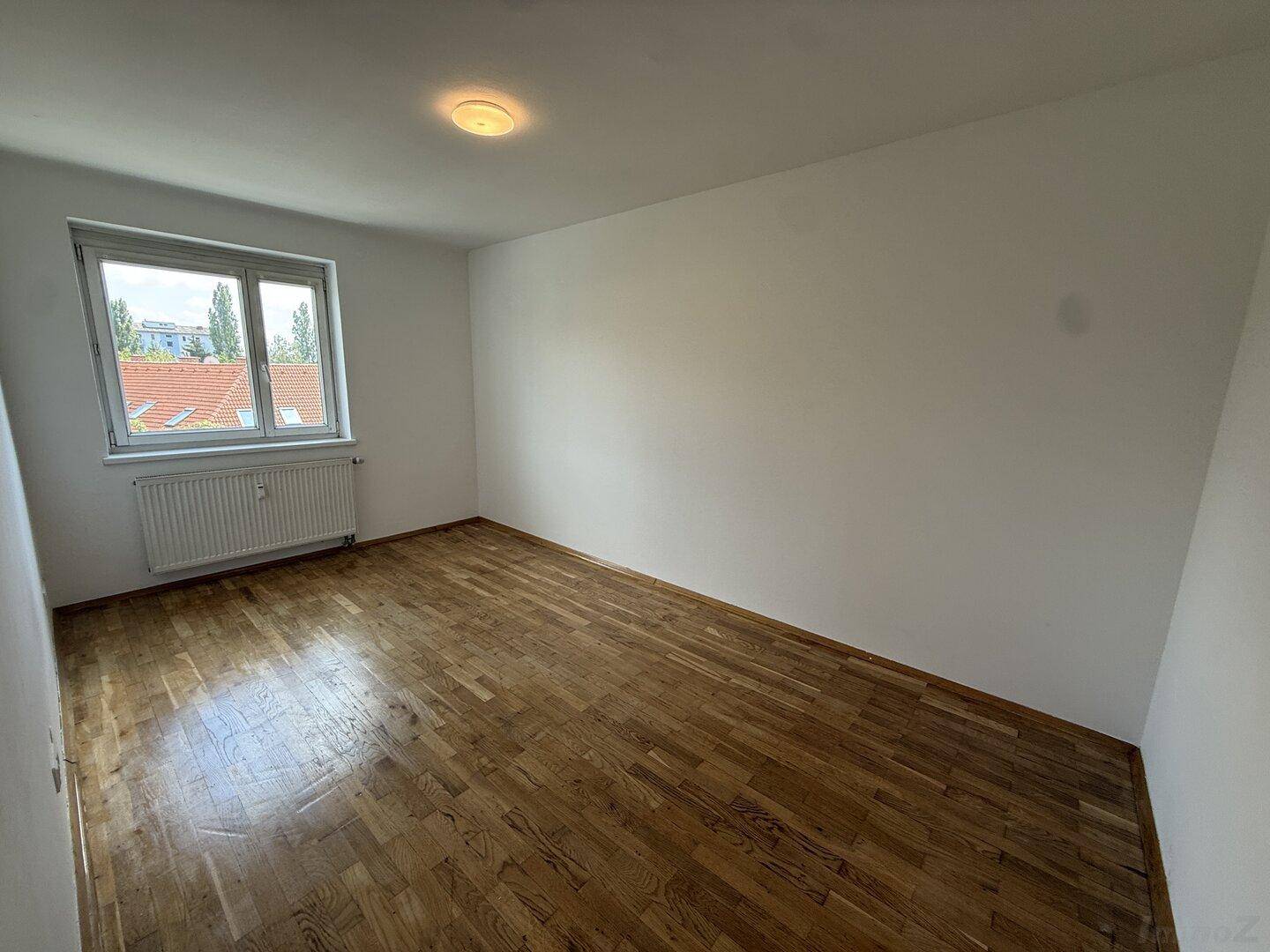 Helles Zimmer mit Holzparkettboden und Fenster, das einen weiten Blick ermöglicht.