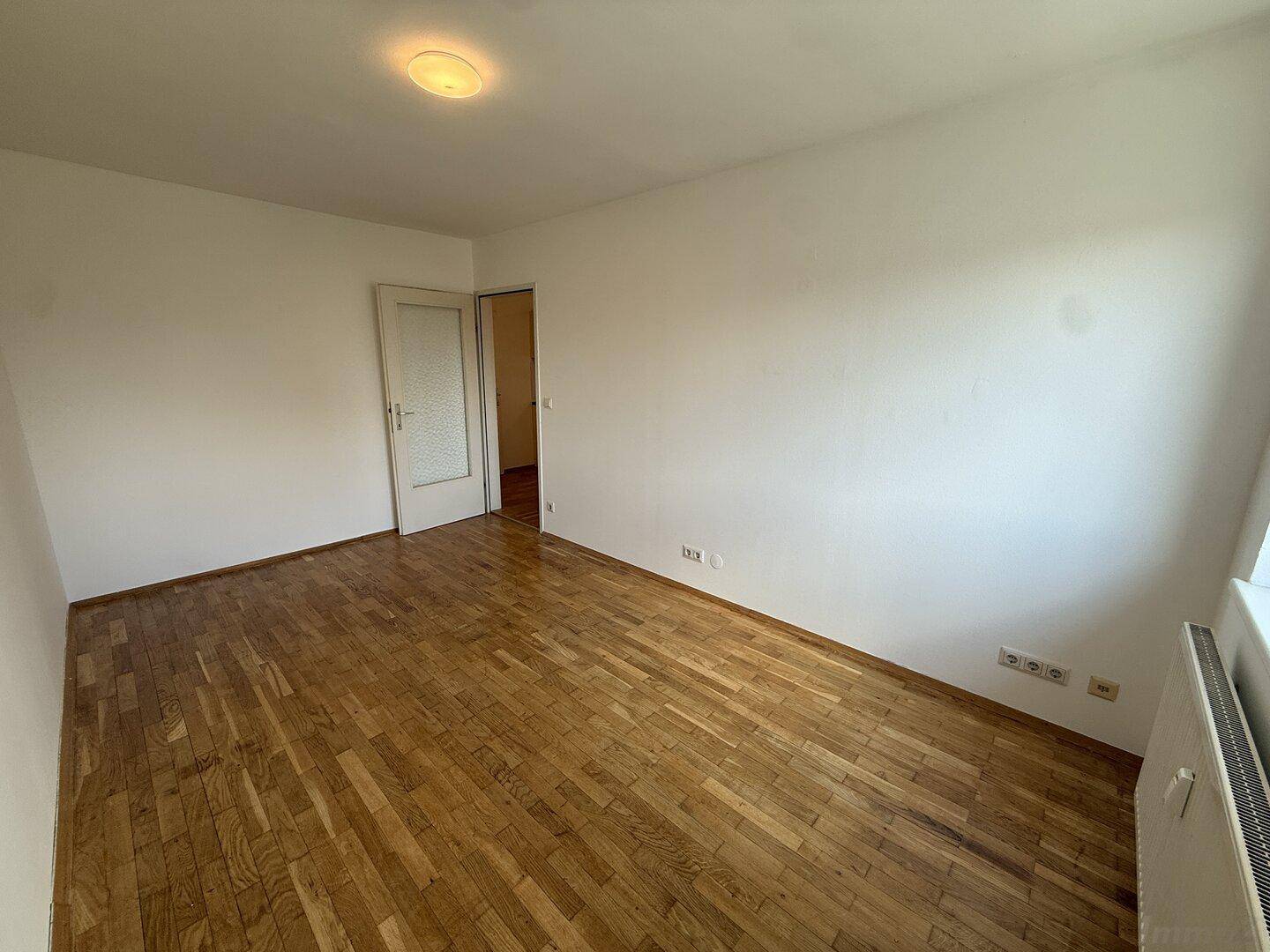 Leeres Zimmer mit Holzparkettboden und Fenster, das viel Tageslicht hereinlässt.