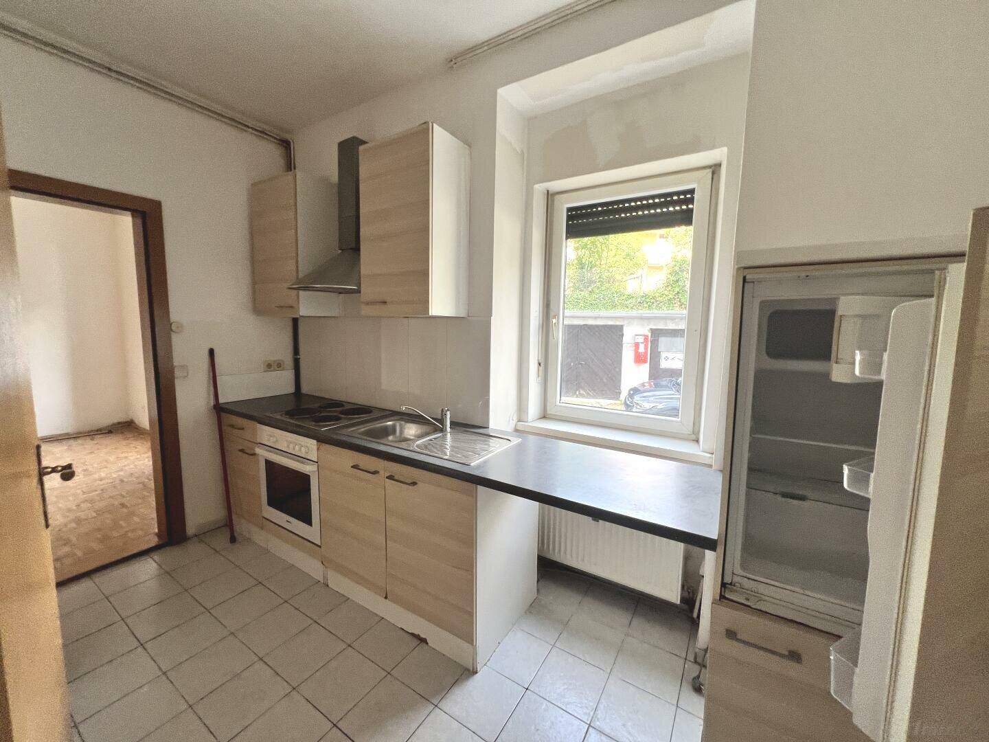 Funktionale Einbauküche mit hellen Holzfronten, Geräten und Fensterblick auf den Außenbereich.