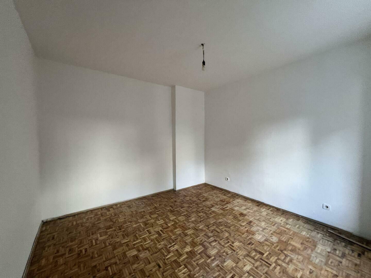 Leeres Zimmer mit Fischgrätparkett und hellen Wänden, bereit zur individuellen Einrichtung.