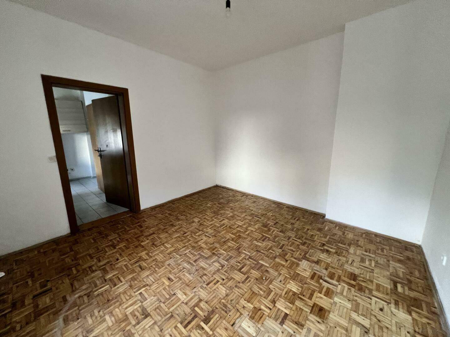 Geräumiges Zimmer mit Fischgrätparkett und Zugang zu weiteren Räumen, ideal für flexible Nutzung.