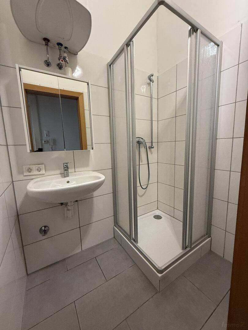 Modernes Badezimmer mit Duschkabine, Waschbecken und Spiegelschrank, hell gefliest und funktional.
