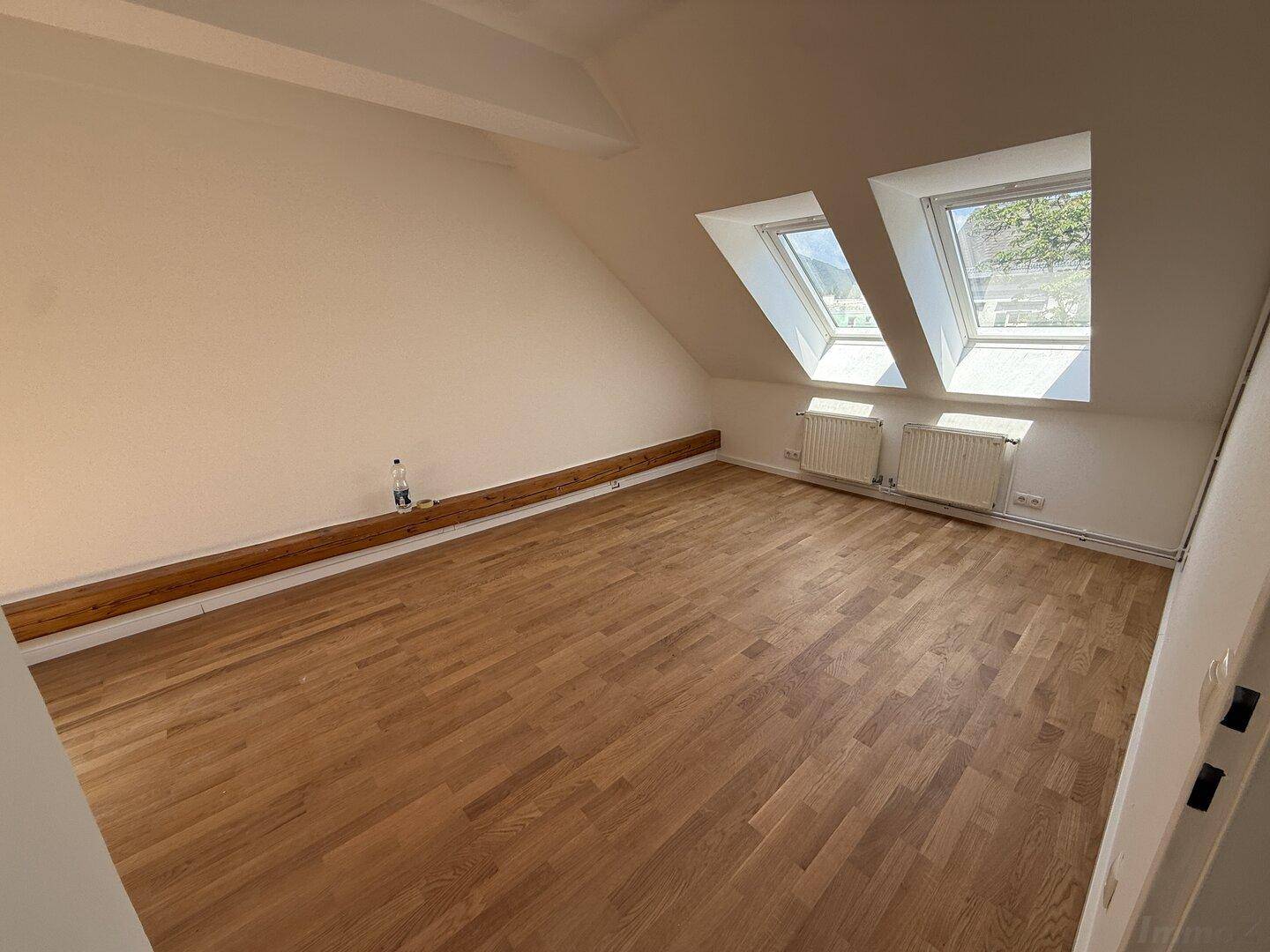 Geräumiges Zimmer im Dachgeschoss mit Holzboden und zwei großen Dachfenstern, sehr hell.