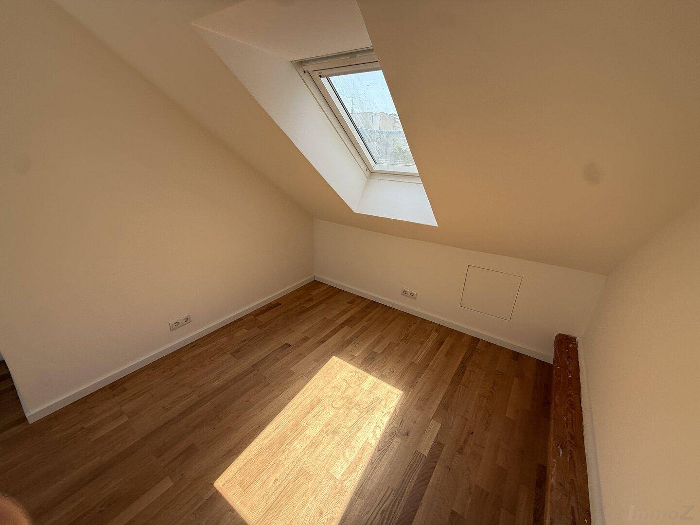 Gemütliches Dachgeschosszimmer mit Holzboden und einem großen Dachfenster, das den Raum erhellt.