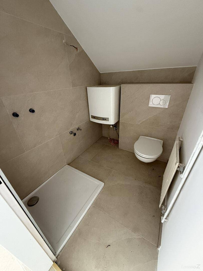 Modernes Badezimmer im Dachgeschoss mit Dusche, WC und beigefarbenen Fliesen.