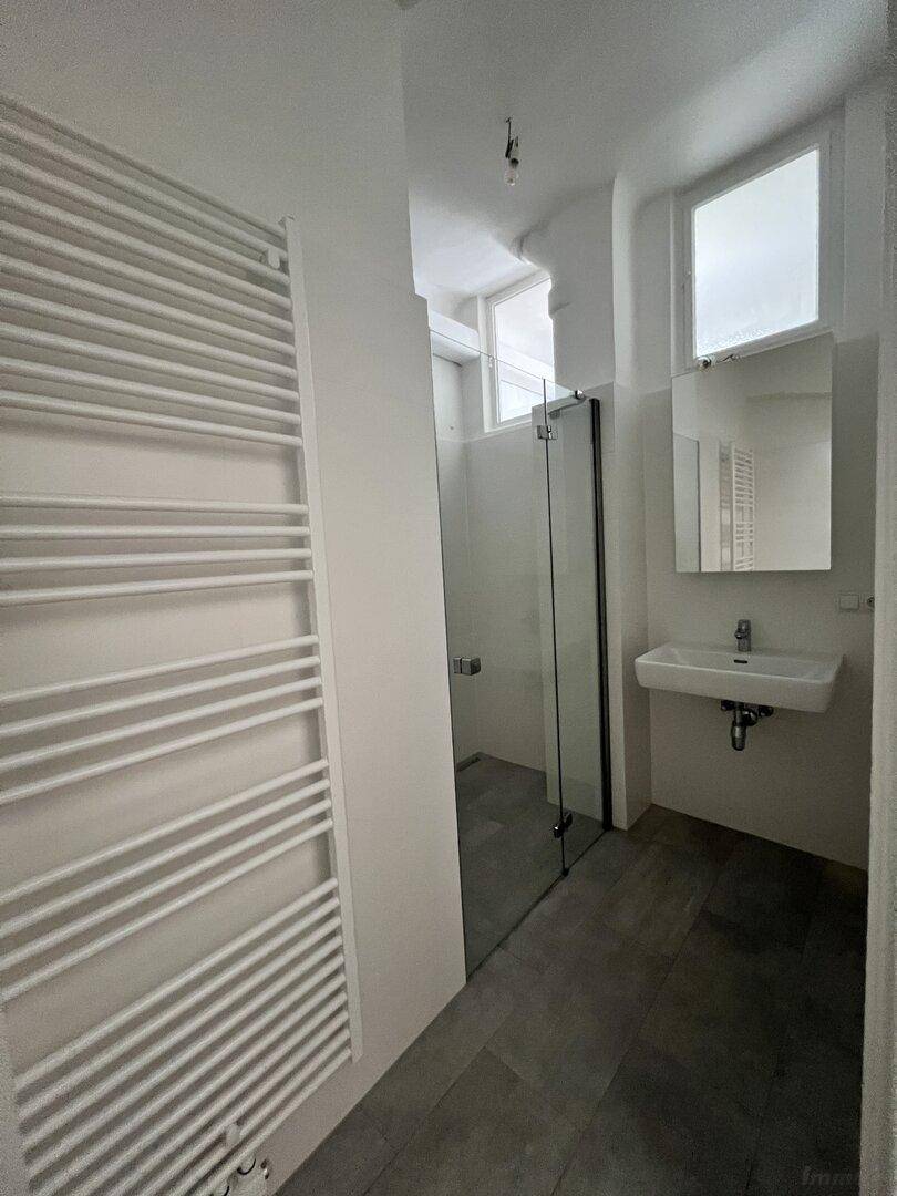 Modernes Badezimmer mit Duschkabine, Waschbecken, Spiegel und beheiztem Handtuchhalter.
