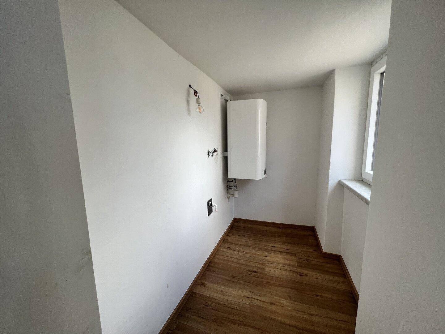Praktischer Hauswirtschaftsraum mit Warmwasserbereiter und Fenster, ideal für Lagerung.